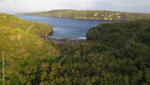 Aerial Sunrise Flying Over Hilly Tropical Forest Revealing Gamat Bay Beach in Nusa Penida, Bali, Indonesia photo