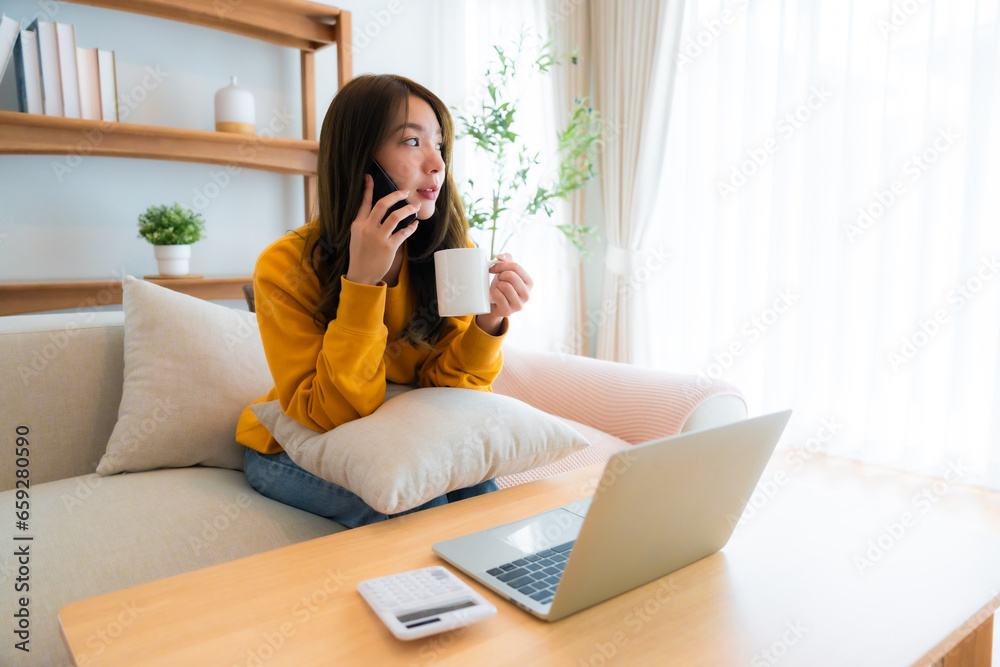 Young Asian female wearing glasses using laptop, working at home in living room, coffee mug on table. Cozy office workplace, remote work Young Asian female wearing glasses using laptop, working at home in living room, coffee mug on table. Cozy office workplace, remote work