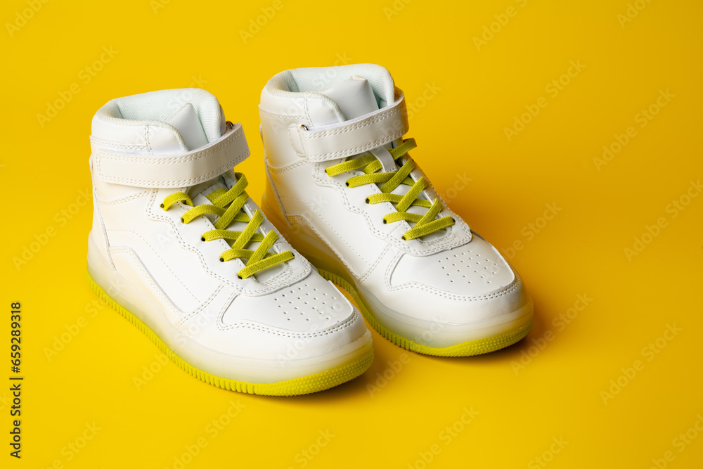 White sneakers with yellow neon laces on yellow background