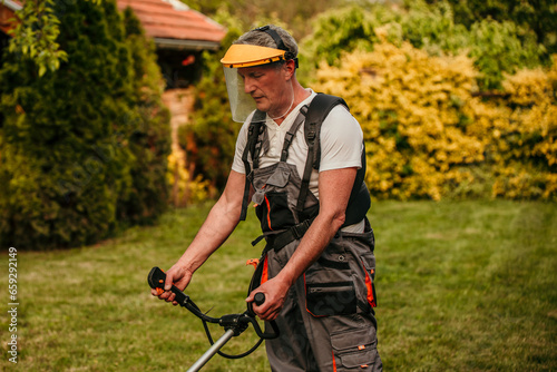 Senior man, equipped in safety gear, skillfully using a grass trimmer to maintain his lush green lawn in his retirement oasis