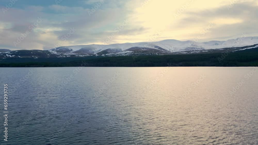 Forwards fly above lake in winter mountain landscape. Snowcapped ridge under cloudy sky at twilight. Scotland, UK Forwards fly above lake in winter mountain landscape. Snowcapped ridge under cloudy sky at twilight. Scotland, UK