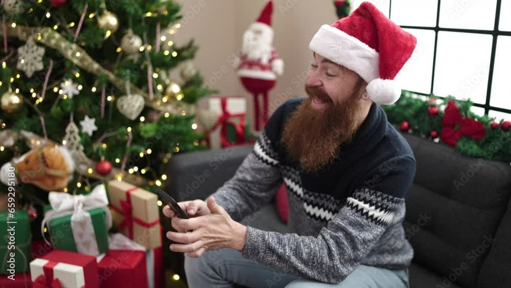 Young redhead man make selfie by smartphone sitting on sofa by christmas tree at home Young redhead man make selfie by smartphone sitting on sofa by christmas tree at home