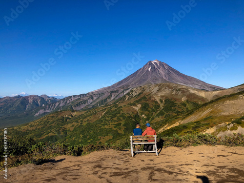 Two people sitting on a wooden bench high in the mountains, view from behind
