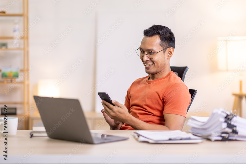 Picture of young asian man using a smartphone and smiling. working at home.accountant Documents data contract report for analysis TAX. Picture of young asian man using a smartphone and smiling. working at home.accountant Documents data contract report for analysis TAX.