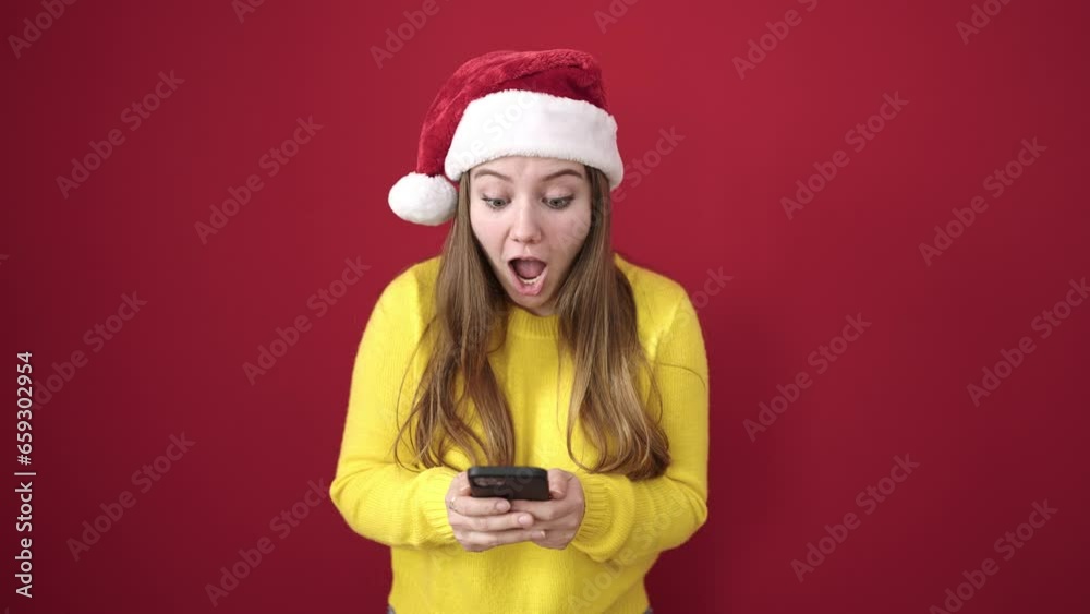 Young blonde woman wearing christmas hat using smartphone over isolated red background Young blonde woman wearing christmas hat using smartphone over isolated red background