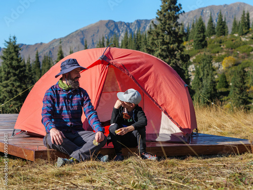 Father and son travel through the mountains. A man and a boy are talking while sitting near a tent