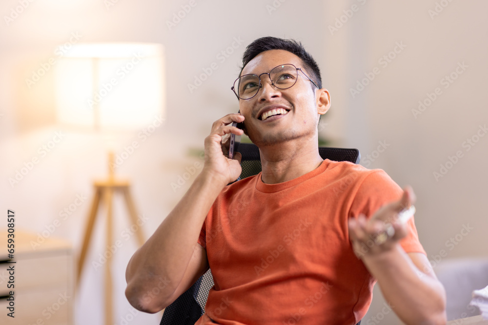 Smiling Asian man writing notes while making phone call and using laptop at home Smiling Asian man writing notes while making phone call and using laptop at home