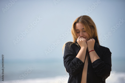 Young woman, blonde and beautiful, wearing a bikini and black shirt, clutching the collar of the shirt, loving herself. Concept purity, virginity, protection.