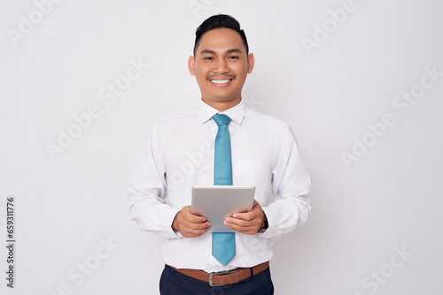 Portrait of smiling happy young Asian man in formal wear holding digital tablet and looking at the camera isolated on white background