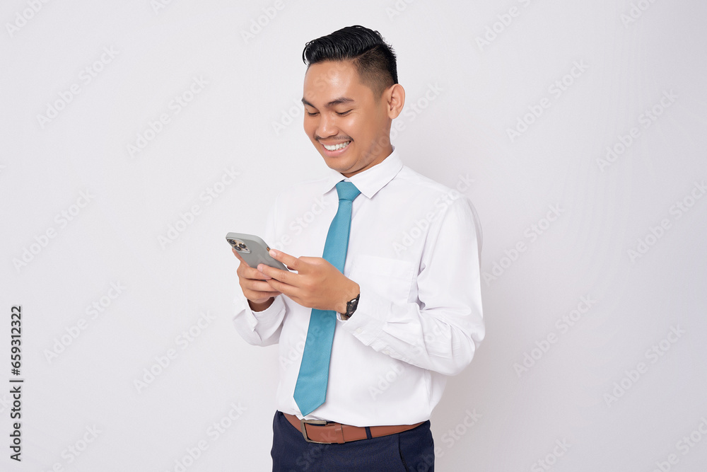Portrait of smiling happy young Asian man in formal wear using mobile phone for texting messages or checking social media isolated on white background