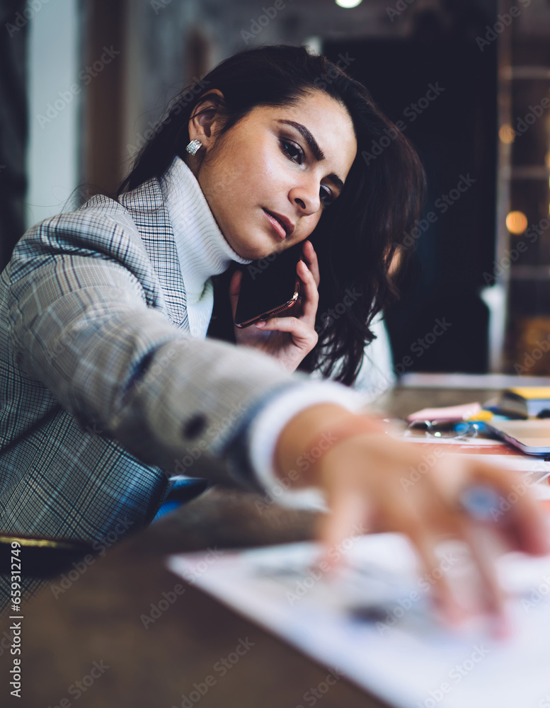 Fototapeta premium Serous female calling on smartphone taking document at workplace