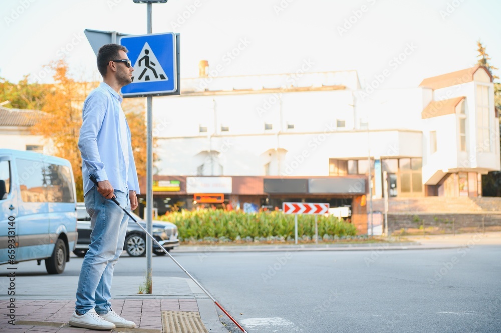young blind man with white cane walking across the street in city