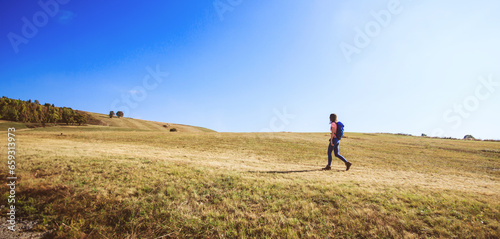 Hiker with backpack walking on rural landscape on sunny autumn day.