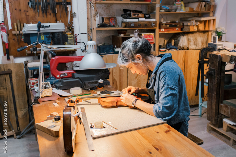 Female craftsperson working on violin at desk in workshop Female craftsperson working on violin at desk in workshop