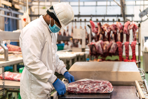 Young butcher packing raw meat in slaughterhouse photo