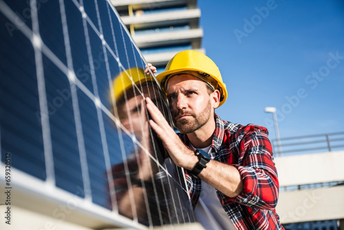 Confident engineer wearing hardhat examining solar panel photo