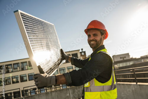 Engineer wearing protective workwear holding solar panel on sunny day photo