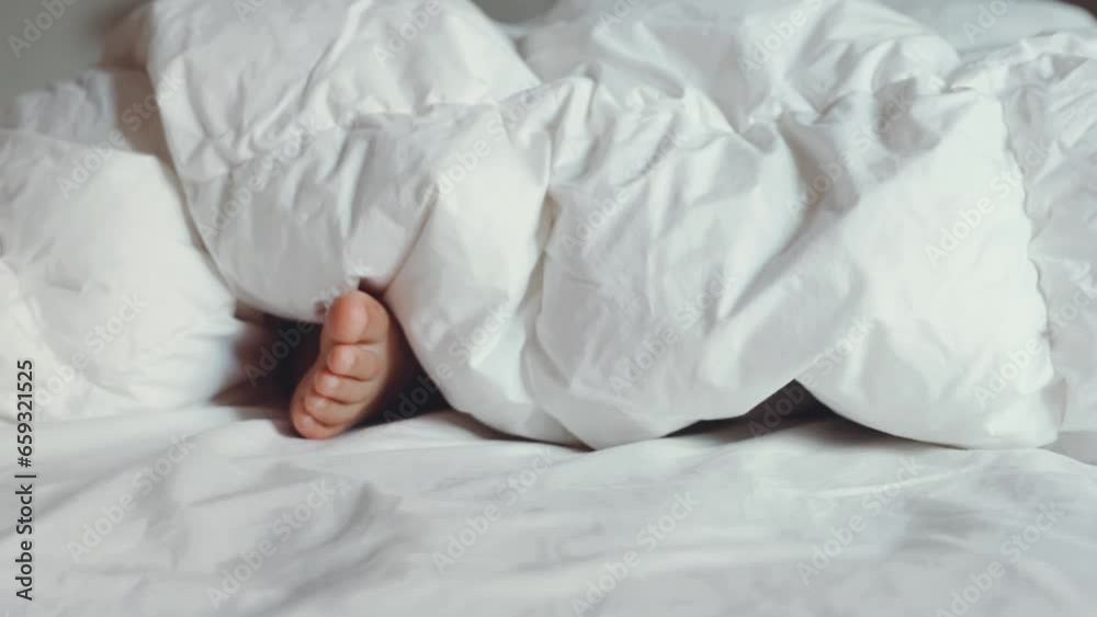Kid barefoot under white fluffy blanket in bed. Child hides feet under warm cotton blanket. Sleep and relaxation in hotel, lazy morning for children. Wake up get ready for school.