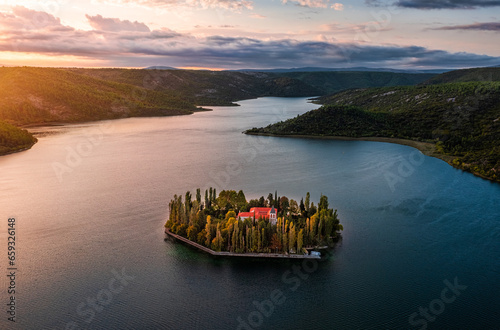 Visovac, Croatia - Aerial panoramic view of Visovac Christian monastery in Krka National Park on a bright autumn morning with dramatic golden sunrise and clouds and clear turquoise blue water