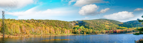 Panoramic aerial view of lake and trees in autumn foliage seaon against blue sky