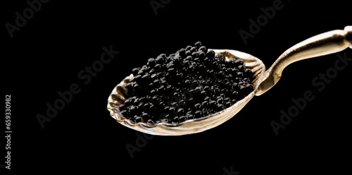 Black Caviar in golden spoon isolated on black background. High quality natural sturgeon black caviar close-up. Delicatessen. Texture of expensive luxury caviar macro shot