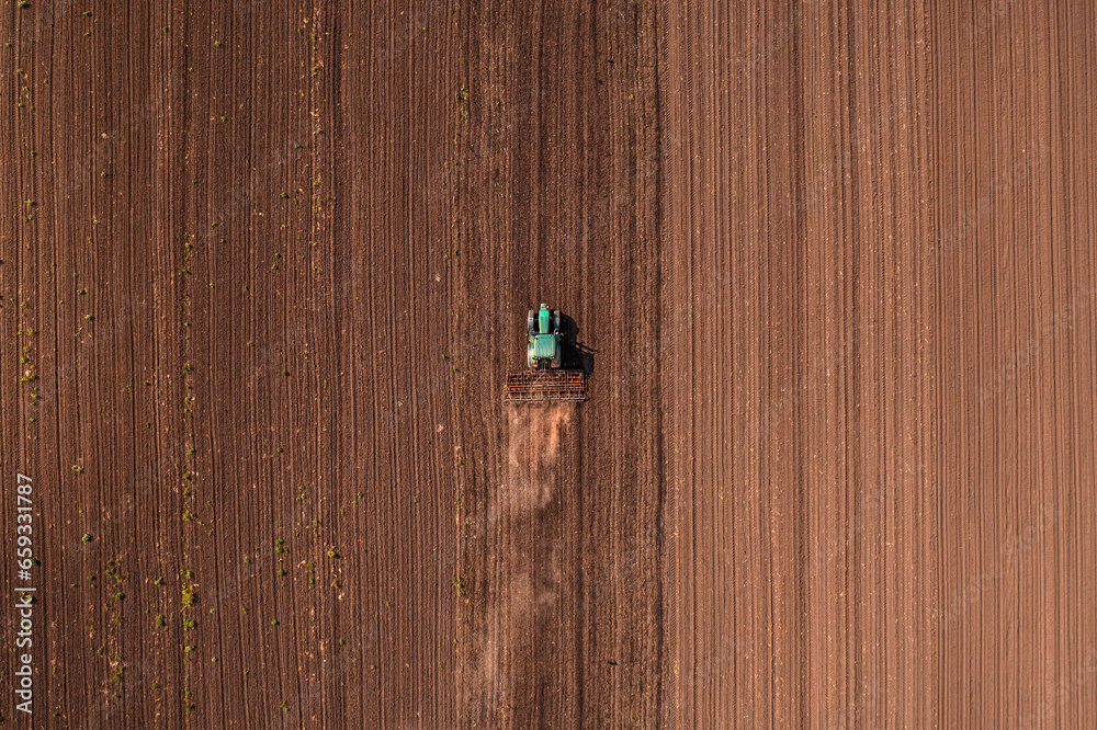Agricultural tractor vehicle with tiller attached performing field tillage before the sowing season, aerial shot seen from the drone pov Agricultural tractor vehicle with tiller attached performing field tillage before the sowing season, aerial shot seen from the drone pov