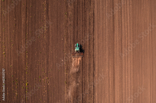 Agricultural tractor vehicle with tiller attached performing field tillage before the sowing season, aerial shot seen from the drone pov