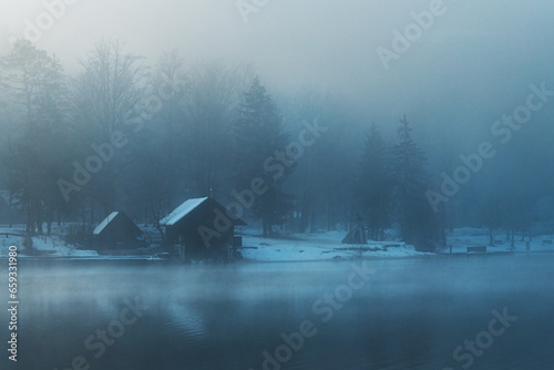 Bohinj lake boathouse at waterfront in foggy winter morning with wooden cabins and piers