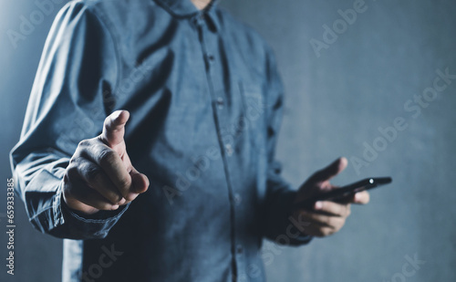 a man holding a smartphone and pointing finger to camera, low-key light, blue color tone, connectivity and technology concept