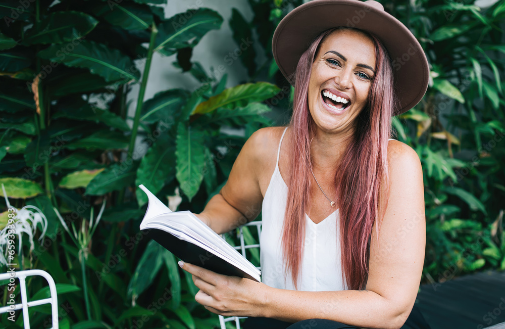 Fototapeta premium Woman laughing reading book at table outdoors