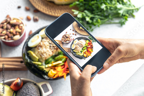 A woman takes a photo of a vegetable bowl on her smartphone.