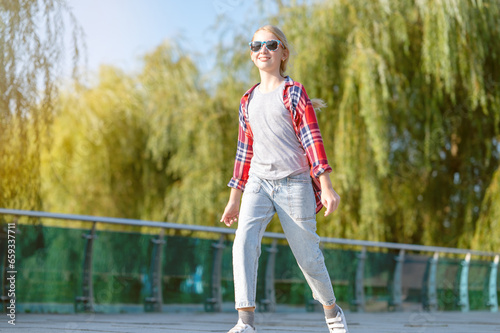 A girl in a plaid shirt jumps and runs along a path in a city park on a sunny summer day. Teenage holiday concept