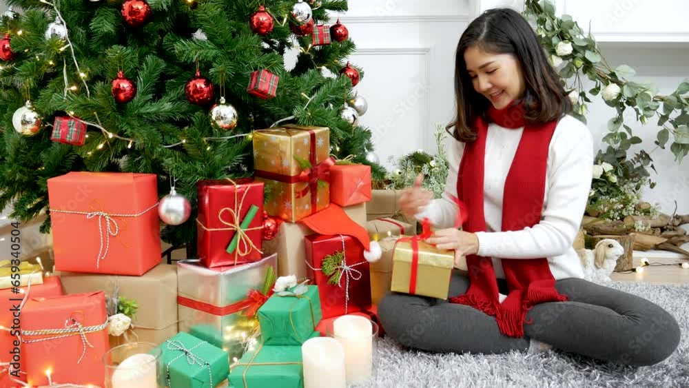 Woman wrapping christmas gift box under xmas tree. Asian woman decor bauble ball christmas tree in xmas holiday winter seasonal celebration. Close up woman hands wrap present gift in cozy living room Woman wrapping christmas gift box under xmas tree. Asian woman decor bauble ball christmas tree in xmas holiday winter seasonal celebration. Close up woman hands wrap present gift in cozy living room