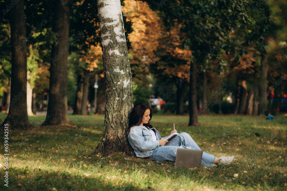 woman under tree with laptop and notepad woman under tree with laptop and notepad