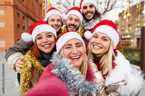 Happy friends wearing santa claus hat celebrating Christmas night together on city street - Group of young people having new year party outside - Winter holidays concept