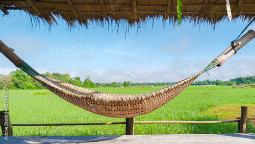 small homestay at the farm with a green rice paddy field in Central Thailand. hammock in front of a wooden bamboo hut looking out over a green rice paddy field in Thailand