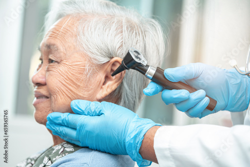 Audiologist or ENT doctor use otoscope checking ear of asian senior woman patient treating hearing loss problem.