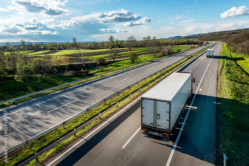 Transportation trucks with trailers on an asphalt highway road in a rural landscape at sunset photo