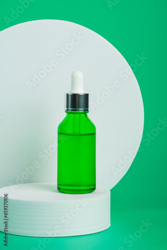 A green glass dropper bottle with stylish props on green background
