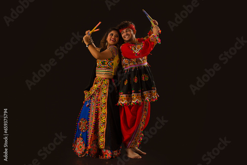 Portrait of happy young couple performing Dandiya Raas on a black background, during Navratri celebrations