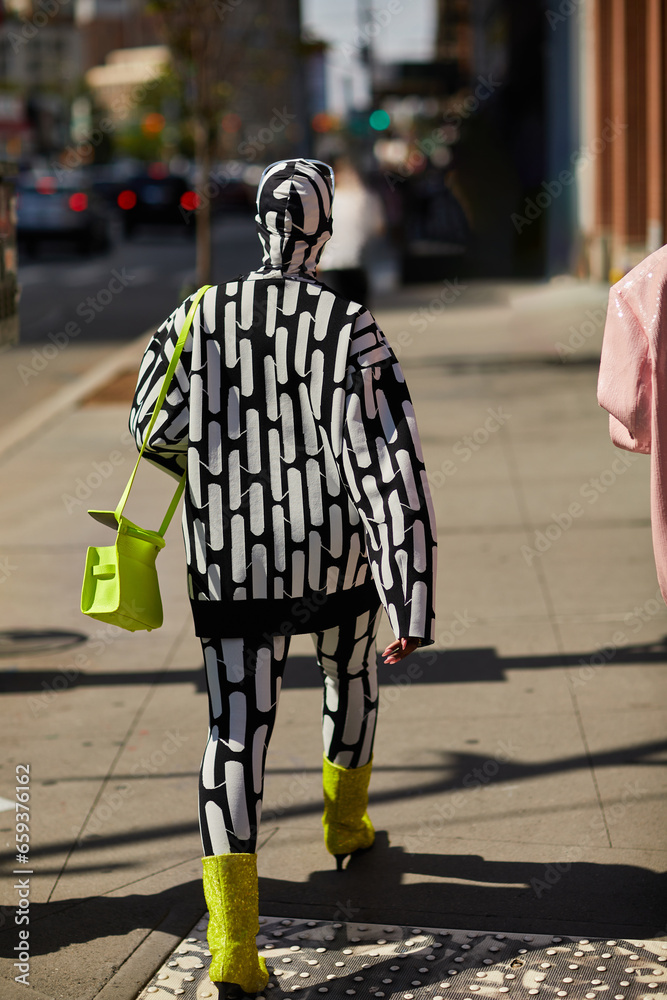 back view of trendy extravagant person walking along street in new york city, urban style
