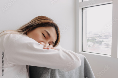 Asian Thai woman sitting on floor near window and closing her eyes, facing down on table alone in apartment room. taking a nap in winter time.