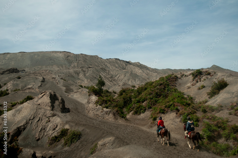 Two people riding horses on pathway to mount base of Bromo crater in Bromo Tengger National Park, East Java, Indonesia. 