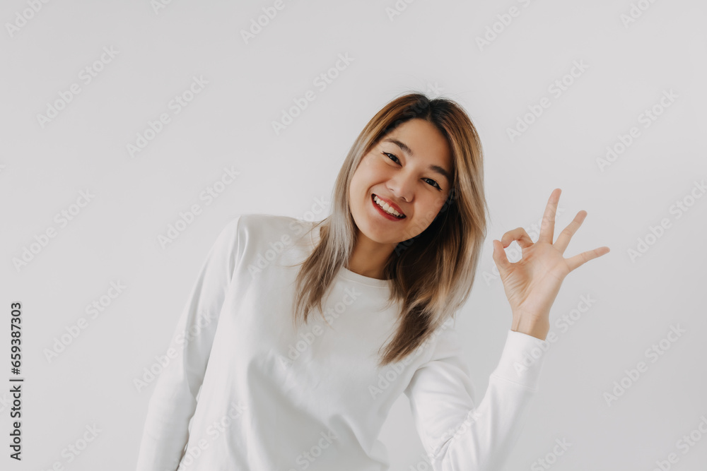 Asian Thai woman smiling and showing okay sign gesture, giving positive feedback, isolated on white background in winter. Asian Thai woman smiling and showing okay sign gesture, giving positive feedback, isolated on white background in winter.