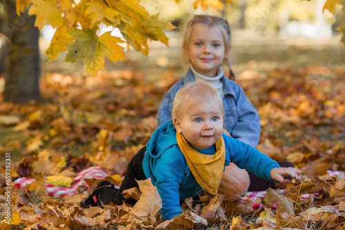 Portrait of a little boy 9 months old and a girl 4 years old outdoors. Happy children in the autumn park with pumpkins. Happy childhood and fatherhood.