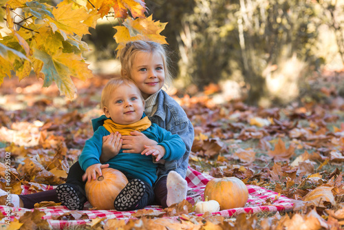 Portrait of a little boy 9 months old and a girl 4 years old outdoors. Happy children in the autumn park with pumpkins. Happy childhood and fatherhood.