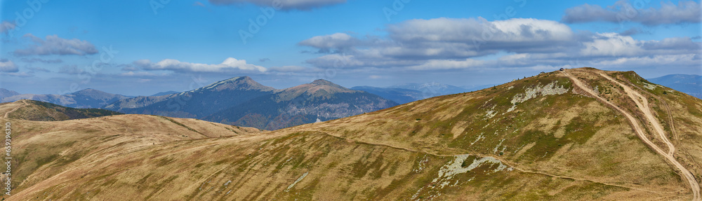 Panorama of a mountain range in the Ukrainian Carpathians in autumn. There is a dirt road on the ridge that is used by off-road vehicles and timber trucks.