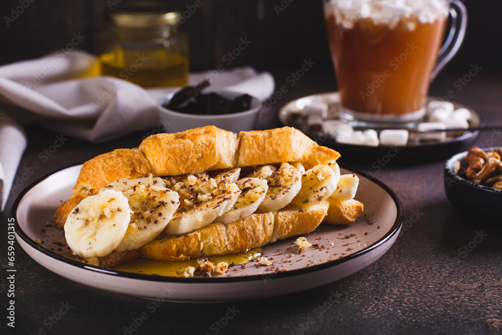 Delicious croissant with banana, honey, chocolate and nuts on a plate on the table