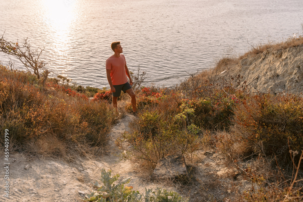 Man in a T-shirt and shorts on the coast among the rocks with warm sun light.