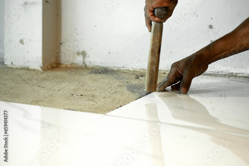 Laying ceramic tiles, close up hands of the worker are laying the ceramic tile on the floor, uses the hammer handle to debug